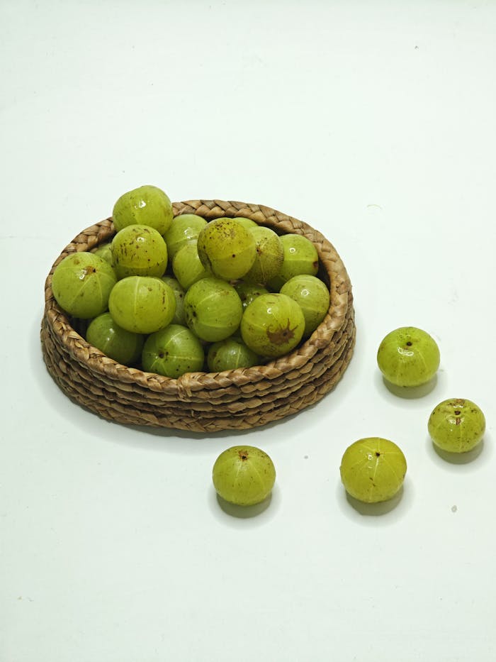 who-we-are A vibrant arrangement of fresh Indian gooseberries (Phyllanthus emblica) in a wicker basket against a white background.